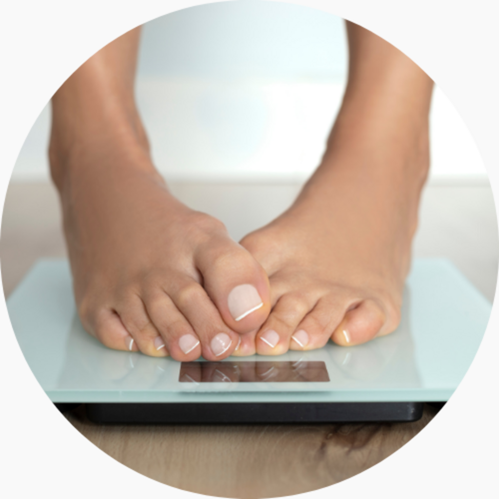Feet standing on a glass digital scale, measuring body weight on a wooden surface