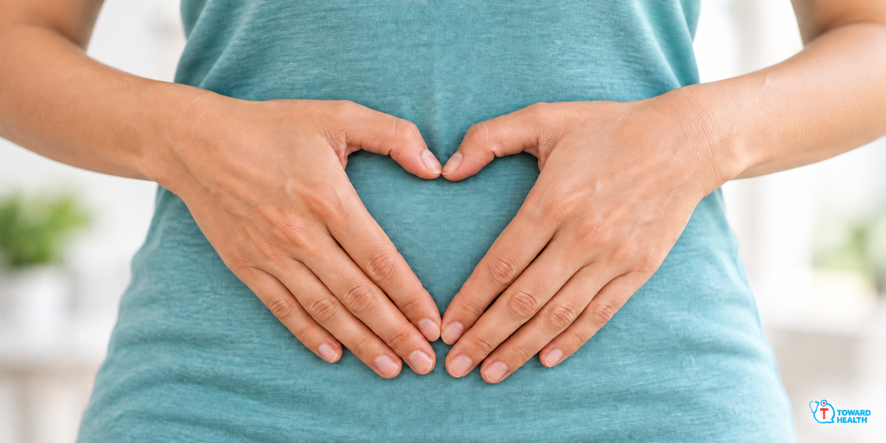 Two hands forming a heart over an abdomen covered by a teal shirt.